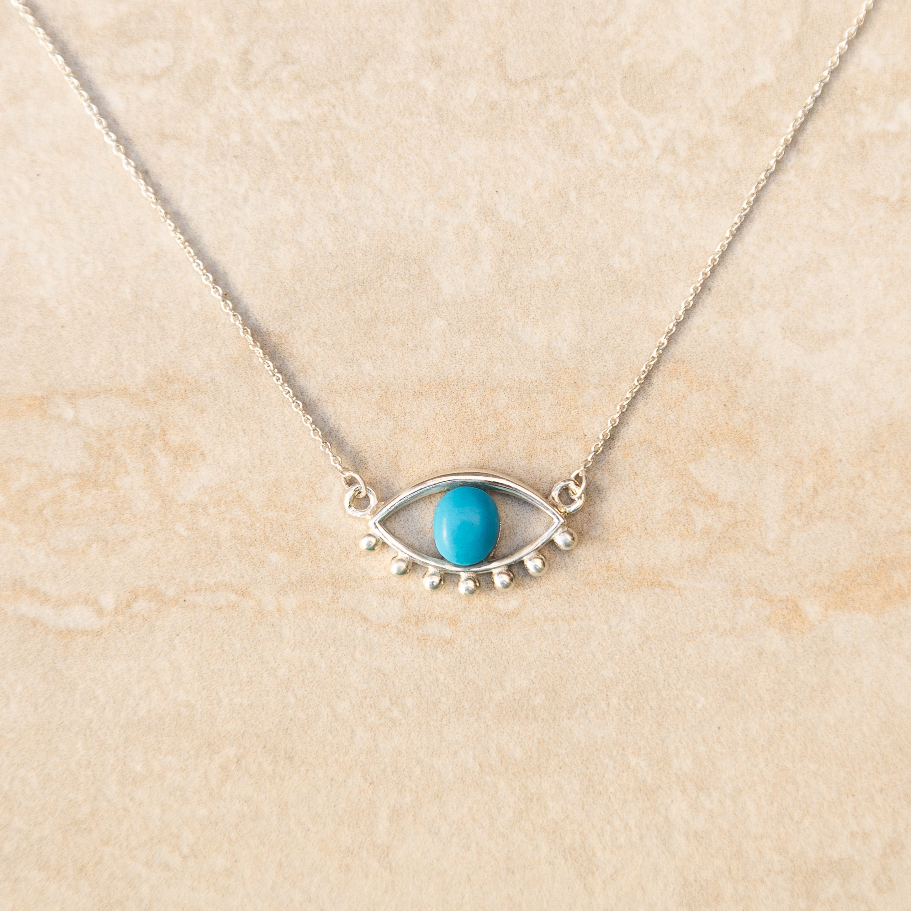 Necklace with eye-shaped pendant and turquoise stone on beige background